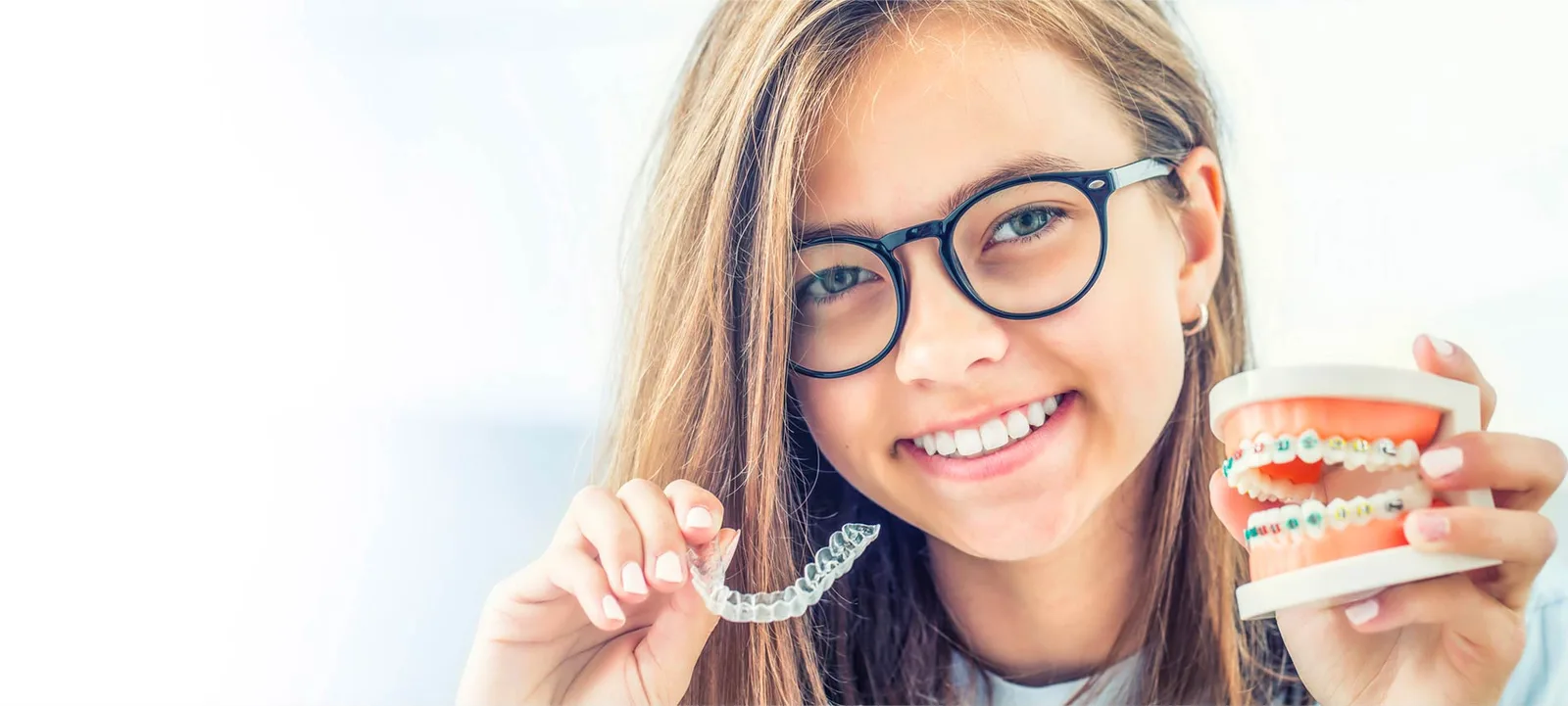 Smiling teen holding a clear Invisalign aligner and a braces model